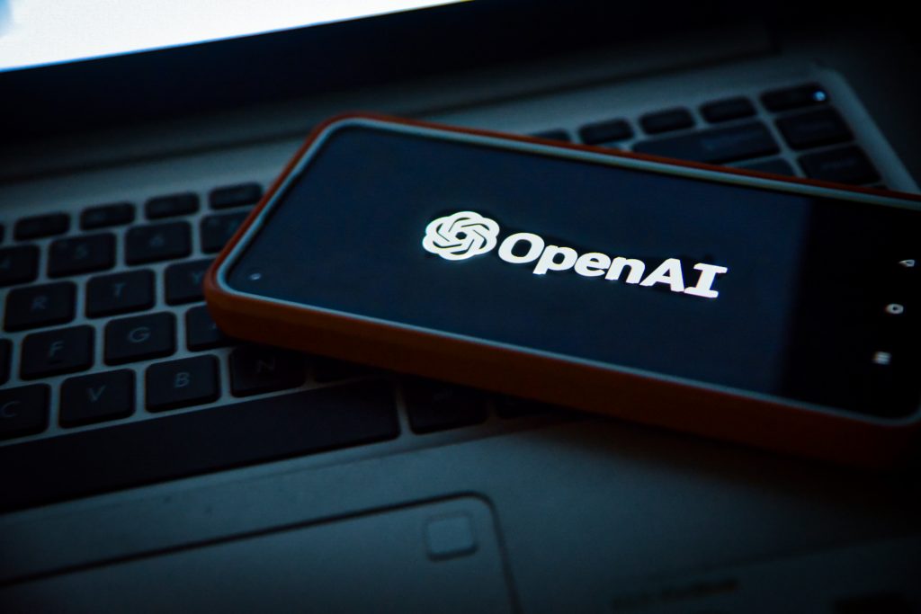 Smartphone displaying the OpenAI logo laying on a laptop keyboard