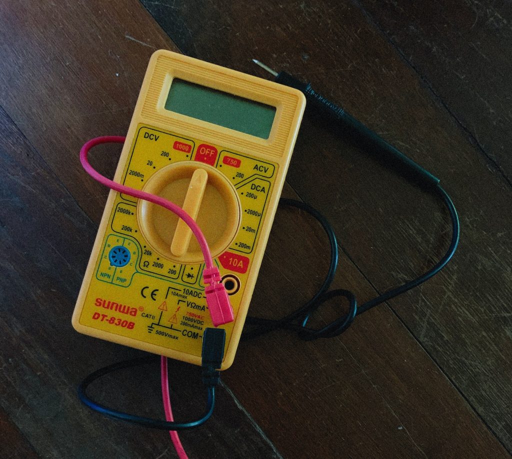 Closeup of yellow digital multimeter with pink and black cables